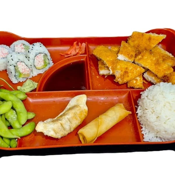 A red bento box filled with sushi, fried chicken, rice, edamame, gyoza, and an egg roll.